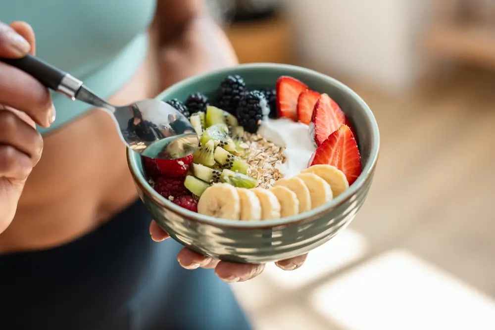 Gros plan sur une femme sportive mangeant un bol de fruits sain dans la cuisine à la maison.
