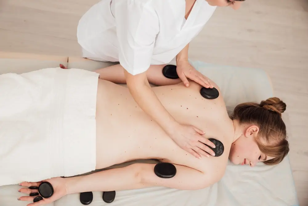 Masseur féminin faisant un massage thérapeutique du dos avec des pierres.